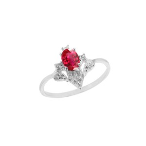 May include: A silver ring with a vibrant, oval-cut, red gemstone at its centre. The gemstone is framed by smaller, clear stones and a decorative silver setting. The ring's band is a simple, polished silver design.
