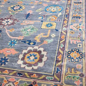 May include: A close-up of a gray rug with a detailed floral pattern. The rug features a central field with various floral motifs in shades of pink, blue, yellow, and purple. The border has a repeating geometric design. The text "Yafiah Rugs" is visible.