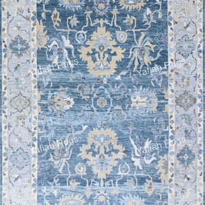 May include: A rectangular area rug with a central field of deep blue, adorned with intricate floral and geometric patterns in shades of beige, light blue, and white. The rug features a detailed border in complementary colors, creating a cohesive design. The text "Yafiah Rugs" is visible.