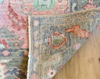May include: Close-up of a distressed, vintage-style rug with a floral pattern. The rug features a color palette of pink, green, and gray. The rug's edge is folded over, revealing the underside with the text "Yatiah Rugs".
