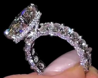 Op de afbeelding: Een schitterende verlovingsring met een grote, ovaal geslepen diamant als middensteen, omringd door een halo van kleinere diamanten. De band is bezet met extra diamanten, wat een sprankelende, luxueuze uitstraling creëert. Op een zwarte achtergrond.