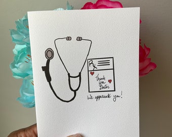 May include: A white card with a black and white illustration of a stethoscope and a prescription pad. The text on the card reads "Thank you Doctor, we appreciate you!"