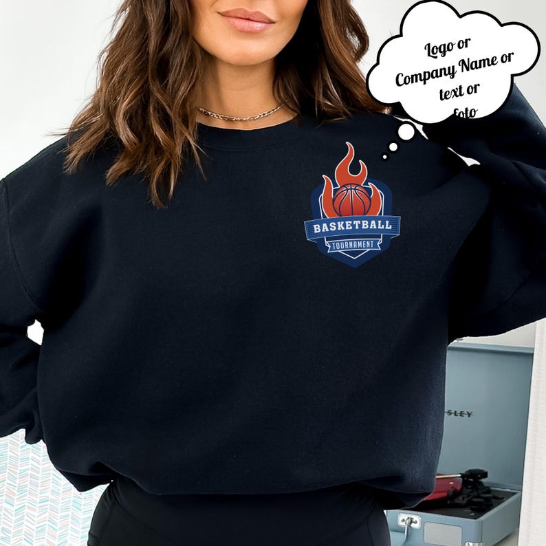 Może przedstawiać: Granatowa bluza z logo turnieju koszyk&oacute;wki. Logo zawiera koszyk&oacute;wkę, płomienie i napis "BASKETBALL TOURNAMENT" w kolorze niebieskim i czerwonym. Bluza jest jednokolorowa i ma okrągły dekolt.