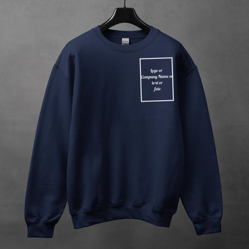 Może przedstawiać: Granatowa bluza z okrągłym dekoltem, zawieszona na czarnym wieszaku. Na piersi biały prostokąt z napisem "logo or Company Name or text or foto". Bluza wykonana jest z miękkiego materiału.