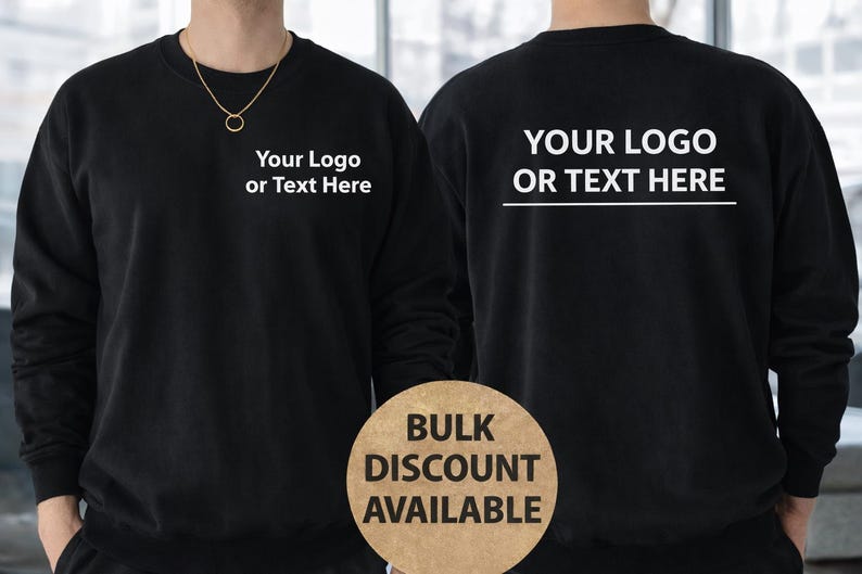 Może przedstawiać: Czarna bluza z napisem "Your Logo or Text Here" z przodu i z tyłu. Z przodu widoczny jest złoty naszyjnik. Okrągły znak z napisem "Bulk Discount Available" znajduje się na dole. Bluza jest w jednolitym czarnym kolorze.
