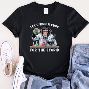 May include: Black t-shirt with a graphic of a chimpanzee in a lab coat pouring liquid into a beaker, with the text "LET'S FIND A CURE FOR THE STUPID". The shirt also features a microscope and two flasks.