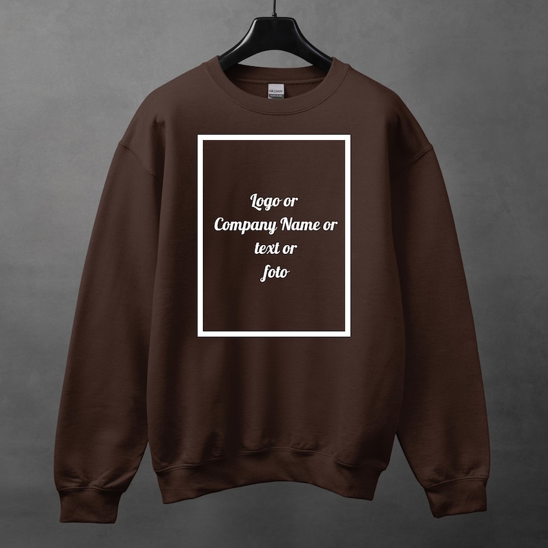 Może przedstawiać: Brązowa bluza z białym prostokątnym wzorem pośrodku. Tekst wewnątrz prostokąta brzmi "Logo lub Nazwa firmy lub tekst lub foto". Bluza wisi na czarnym wieszaku.