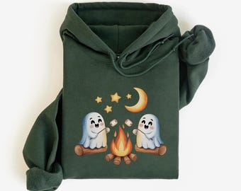 May include: A dark forest green hooded sweatshirt featuring a graphic print of two white cartoon ghosts sitting on logs by a campfire, roasting marshmallows on sticks under a yellow crescent moon and several small yellow stars in the night sky.