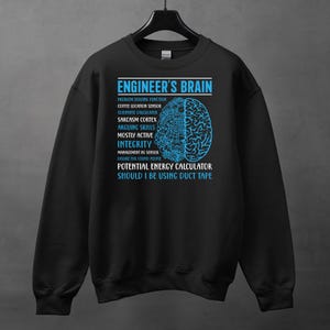 Op de afbeelding: Zwart sweatshirt met een blauw grafisch ontwerp met de tekst "ENGINEER'S BRAIN" en een hersendiagram. Het ontwerp bevat humoristische beschrijvingen van de hersenfuncties van een ingenieur.