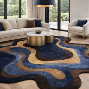 May include: A modern living room featuring a large, abstract-shaped area rug with a wavy design in shades of blue, brown, and tan. The rug sits on a hardwood floor, complementing the neutral-toned furniture and decor.