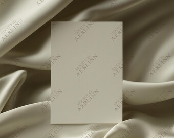 Puede incluir: Una tarjeta rectangular en blanco está centrada sobre un fondo de tela fluida de color crema. La tela tiene un brillo sutil y está drapeada en suaves pliegues. La tarjeta tiene el texto "MOCKUP BY AERLINN" repetido en su superficie.