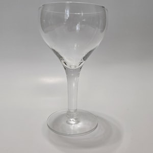 Puede incluir: Una copa de cristal transparente con un cuenco redondeado, un tallo delgado y una base circular. El recipiente está fabricado en cristal liso y transparente con un diseño sencillo, mostrando una amplia abertura y un pie estable.