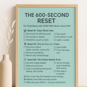 May include: A framed print with a light teal background features the text "THE 600-SECOND RESET" and instructions for quick tasks. The text is in a dark gray font. A white vase with dried flowers sits to the left of the frame.