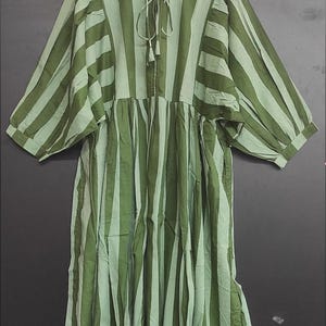 May include: A green and light green striped dress with a round neckline and three-quarter sleeves. The dress features a tie detail at the neckline and a gathered skirt. The fabric appears to be lightweight, suitable for warmer weather.