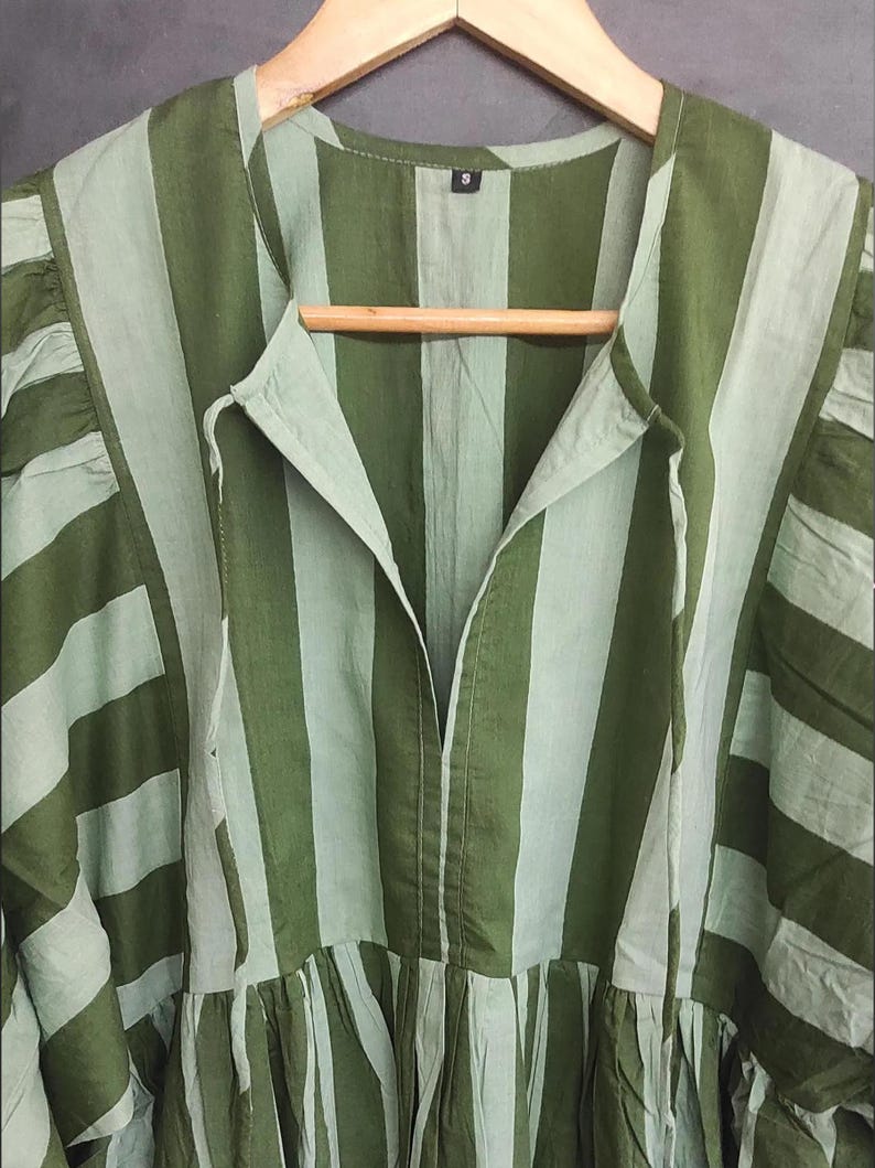May include: A green and light green striped dress with a V-neckline and a gathered skirt. The dress is hanging on a wooden hanger. The fabric has a soft, flowing appearance.