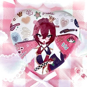 May include: A heart-shaped pin featuring an anime-style character with dark red hair and a small crown. The background is white with scattered pink and red doodles, including hearts, stars, and a checkered pattern. The character wears a white and dark blue outfit.