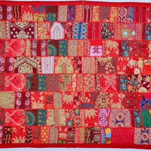 May include: A red patchwork textile with a red border. The textile is made up of numerous squares and rectangles in various shades of red, featuring patterns such as floral, paisley, and geometric designs. It is likely a decorative item, possibly a wall hanging.