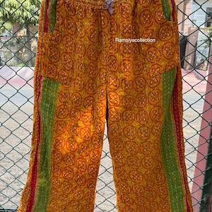 Può includere: Pantaloni gialli fantasia con dettagli rossi e verdi. I pantaloni presentano un motivo circolare ripetuto e sono appesi a una gruccia nera. Il testo "Ramsiyacollection" è visibile.