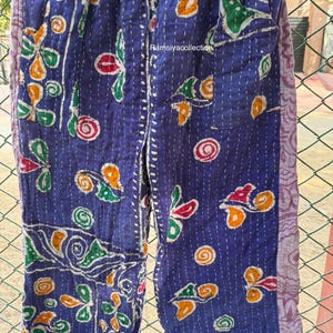 May include: Blue patchwork trousers with colourful floral and swirl patterns. The trousers have a drawstring waist and are decorated with white stitching. The text "Ramsiyacollection" is visible.