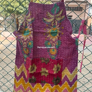 Pode incluir: Avental feito à mão com fundo roxo e bordados florais. O avental tem um bolso com desenhos florais e um padrão zigue-zague amarelo e rosa na parte inferior. O texto "Ramsiyacollection" é visível.