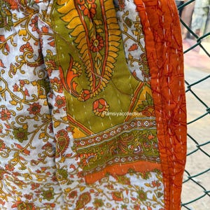 Op de afbeelding: Close-up van kleurrijke patchworkstof met bloemen- en paisley-patronen in wit, oranje en groen. De stof is aan elkaar gestikt met witte draad. De tekst "Ramsiyacollection" is zichtbaar.