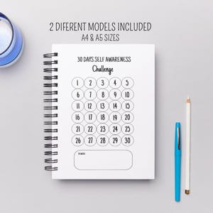 Könnte beinhalten: Ein weißes Spiralnotizbuch mit einem 30-Tage-Selbstbewusstseins-Challenge-Layout. Der Text "2 VERSCHIEDENE MODELLE ENTHALTEN A4 & A5 GRÖSSEN" steht oben. Ein blauer Stift und ein weißer Bleistift liegen daneben.