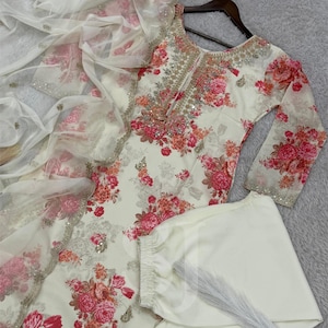May include: Off-white floral print salwar kameez set. The ensemble includes a long-sleeved tunic, matching pants, and a sheer dupatta. The tunic and dupatta feature a vibrant floral pattern in shades of pink and orange, with intricate sequin and bead embellishments.