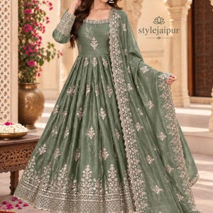 Könnte beinhalten: Ein bodenlanges Anarkali-Kleid in Salbeigrün mit quadratischem Ausschnitt, langen Ärmeln und aufwendiger silberner Stickerei auf dem Oberteil, dem Rock und den Manschetten. Das Set enthält einen passenden Dupatta mit breitem Stickrand.