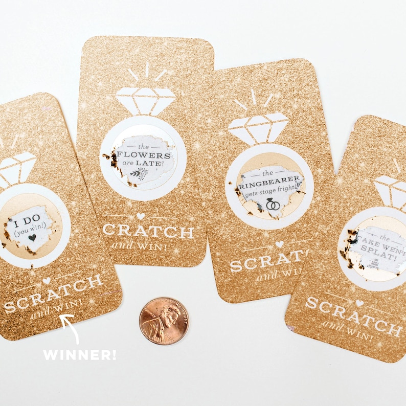 May include: Four gold glitter scratch-off cards with a diamond ring icon and the text "Scratch and Win!"  The cards have different messages underneath the scratch-off area, including "I Do (you win!)", "The Flowers are Late!", "The Ringbearer gets stage fright", and "The Cake Went Splat!"
