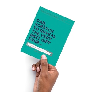 May include: A teal scratch-off card held by a hand, with the text "DAD, SCRATCH TO REVEAL THE VERY BEST GIFT EVER..." and "RANDOM SCRATCH OF KINDNESS" printed on it. The card has a scratch-off area with the text "It's meeeeeeeeeee! Love you, dad."