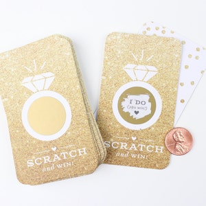 May include: Two gold glitter scratch-off cards with a ring and diamond design. The text on the cards reads "Scratch and Win!" and "I Do (you win!)"