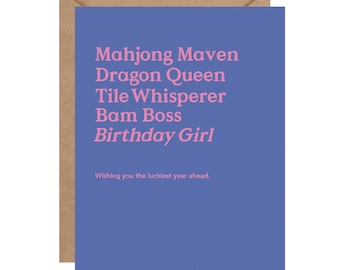 May include: A greeting card with a blue background and a brown envelope. The card features pink text that reads "Mahjong Maven, Dragon Queen, Tile Whisperer, Bam Boss, Birthday Girl." The bottom of the card says, "Wishing you the luckiest year ahead."