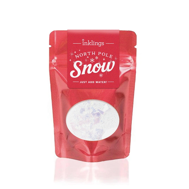 May include: A red stand-up pouch labeled Inklings North Pole Snow with a circular clear window revealing white powder inside. The label features white text that reads North Pole Snow and Just Add Water, decorated with small white snowflake icons.