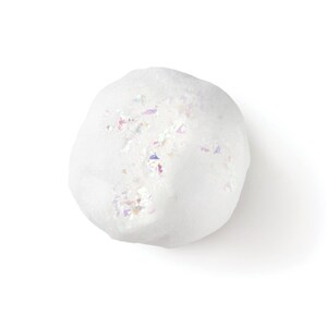 May include: A round, white bath bomb with a textured, porous surface. The top of the sphere is embedded with small, iridescent, multi-colored glitter flakes that reflect light, creating a shimmering effect against the matte white base material.
