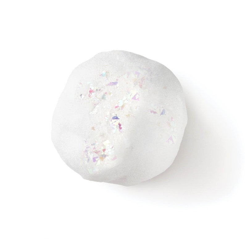 May include: A round, white bath bomb with a textured, porous surface. The top of the sphere is embedded with small, iridescent, multi-colored glitter flakes that reflect light, creating a shimmering effect against the matte white base material.