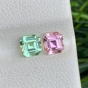 Könnte beinhalten: Zwei quadratisch geschliffene Edelsteine. Einer ist hellgrün, der andere hellrosa. Beide Edelsteine haben ein facettiertes Design und werden auf einer weißen Oberfläche präsentiert. Die Edelsteine sind wahrscheinlich für die Schmuckherstellung.