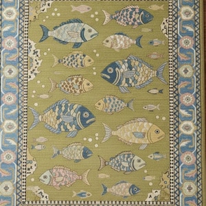 May include: A rectangular rug with a repeating fish pattern. The rug features various fish in shades of blue, tan, and pink on a green background. A blue and pink floral border frames the design. The rug has a fringed edge.