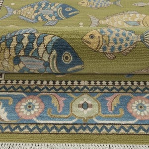 May include: A green area rug with a repeating pattern of stylized fish in shades of blue, yellow, and beige. The rug has a detailed border with floral and geometric designs in blue, pink, and green, and a fringe.