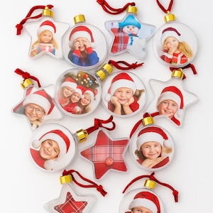 May include: A collection of clear Christmas ornaments in round and star shapes, each featuring a photo of a child wearing a Santa hat. Some ornaments have red plaid patterns. Red ribbons and gold caps complete the festive look.