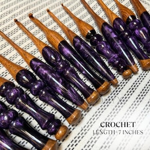 May include: A collection of crochet hooks featuring wooden shafts and ergonomic handles made of marbled purple resin. Each hook measures 7 inches in length. The handles have a contoured, multi-bulb shape, and the hooks are arranged diagonally.