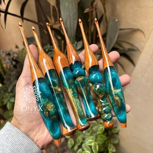 May include: Six handcrafted crochet hooks featuring polished wooden handles and translucent teal resin sections with swirling gold-colored inclusions. Each hook has a tapered metal tip and a unique, ergonomic shape with varying contours.