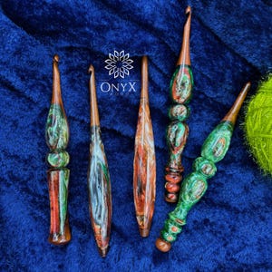 May include: Five handcrafted crochet hooks featuring polished wooden shafts and decorative handles made from swirling resin in shades of green, red, and white. The logo Onyx Wood is printed in white text above the center of the collection.
