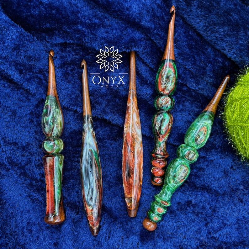 May include: Five handcrafted crochet hooks featuring polished wooden shafts and decorative handles made from swirling resin in shades of green, red, and white. The logo Onyx Wood is printed in white text above the center of the collection.