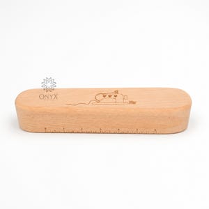 Op de afbeelding: Een lichtgekleurde houten liniaal met een afgeronde rechthoekige vorm. De liniaal heeft een lasergeëtst ontwerp van een naaimachine met harten en de tekst "ONYX WOOD". De liniaal heeft centimeter markeringen.