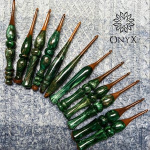 Peut inclure: Un ensemble de dix crochets avec des manches en résine vert émeraude marbré et des tiges en bois brun foncé. Chaque manche présente un motif tourbillonnant unique dans des tons vert profond et doré. Le texte ONYX WOOD est visible sur les manches.