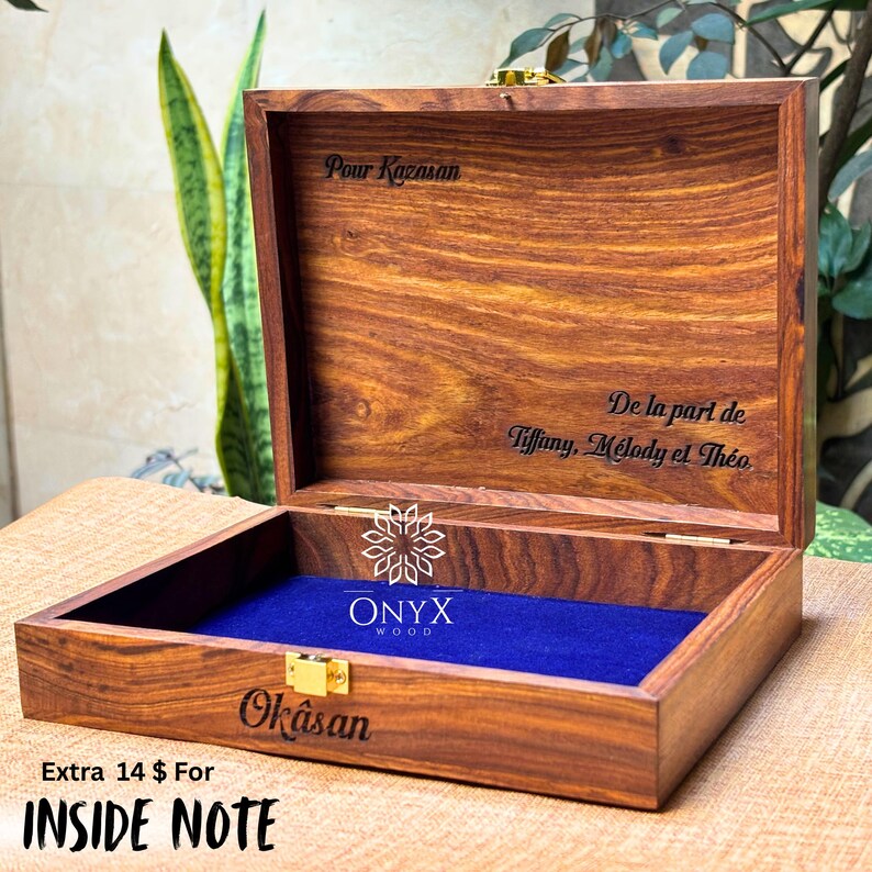 May include: Open wooden box with a blue velvet interior. The box is engraved with the words "Pour Kazasan", "Okasan", and "De la part de Tiffany, M&eacute;lody et Th&eacute;o". The box has a gold-colored clasp and the Onyx Wood logo.