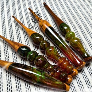 May include: A collection of handcrafted crochet hooks with wooden handles and colorful resin accents. The hooks feature a variety of colors, including green, brown, and amber. The logo "ONYX WOOD" is visible.