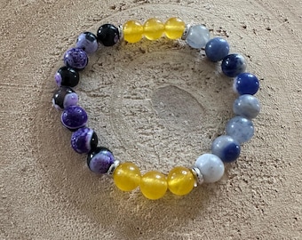 May include: A beaded bracelet featuring a variety of colorful gemstones. The bracelet includes purple, black, yellow, and blue beads, strung together with silver-colored spacers. The bracelet is displayed on a light brown wooden surface.