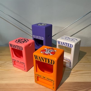 May include: Four rectangular plastic storage boxes in pink, purple, orange, and white. Each box features a front cutout, the word WANTED, and the text DEAD OR ALIVE. The tops display various graphic symbols, including skull and crossbones icons.