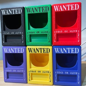 Op de afbeelding: Zes kleurrijke, rechthoekige dozen met het woord "WANTED" in witte blokletters bovenaan. Daaronder staat de tekst "DEAD OR ALIVE". De dozen zijn zwart, groen, rood, paars, geel en blauw.